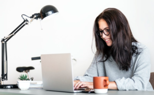 woman wearing jacket working on her laptop with coffee mug on table
